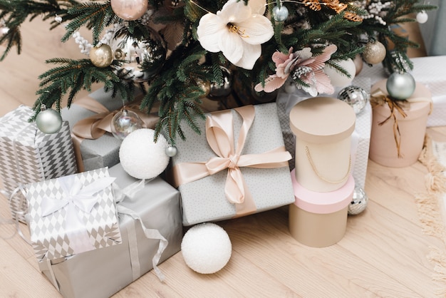 Bright silver gifts with bows under the Christmas tree on the floor