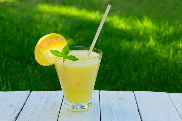 Bright smoothie made from melon with mint and lemon on a background of fresh green grass