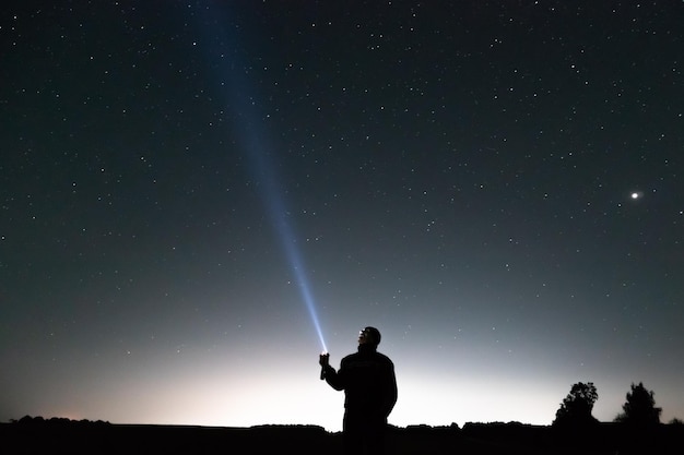 Bright stars and constellations in the night sky The silhouette of a man against the background of the starry sky A man shines a lantern into the sky and tries to illuminate the stars