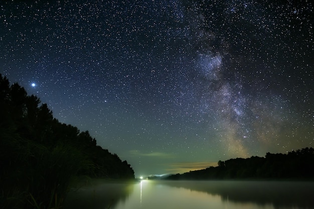 Bright stars of the milky way in the night sky over the river\
with fog. wonderful place for landscape.