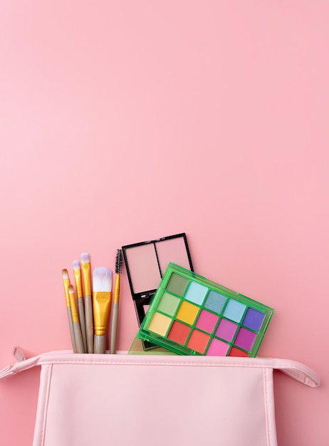 Bright summer eyeshadow palette and makeup products in pink cosmetic bag on pink background