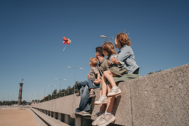 Bright summer photo with a happy family. Parents with children look at balloons. Cozy family walk on the beach