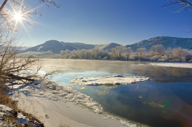 Sole splendente nel cielo senza nuvole. fiume gelido dalle rive collinari e grandi banchi di ghiaccio.