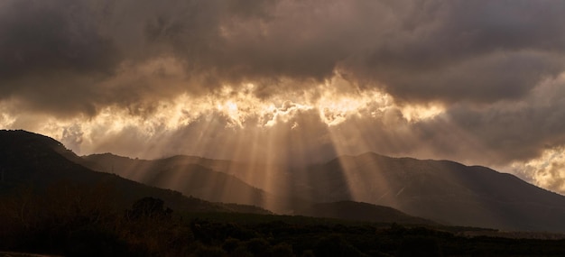 Bright sunlight shining through hole of clouds to dark scene of mountain valley range before sunset