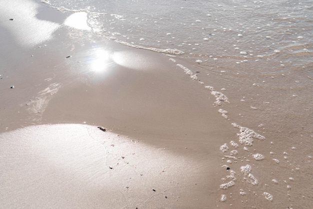 Bright sunny reflection on wet sandy beach with sea waves washing the shore in sunbeams Empty beach coastal feature