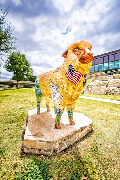 A bright sunny sky illuminates a sheep statue in front of the San Angelo Visitor Center Clouds drift