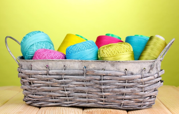 Bright threads in basket on wooden table on green background