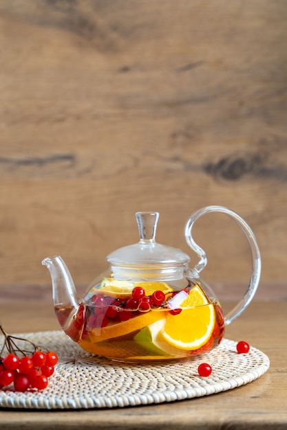 Bright vitamin tea with fruit in a glass teapot on the table on a wooden background closeup