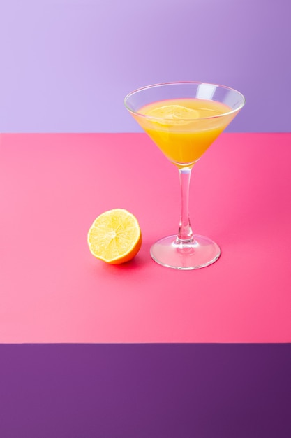 Bright vivid composition with cocktail glass of yellow beverage and fresh lemon placed on colorful background