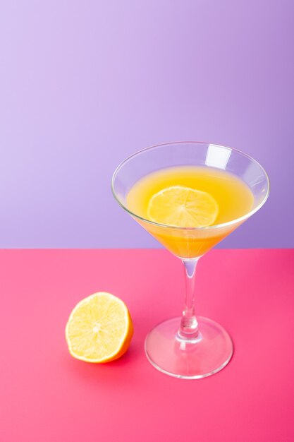 Bright vivid composition with cocktail glass of yellow beverage and fresh lemon placed on colorful background