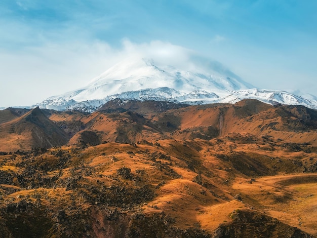 秋の岩の台地の上のエルブルス山の明るい白い雪のピーク 秋のエルブルス コーカサス山脈の秋 白い雪の大きな山々 雪の峰