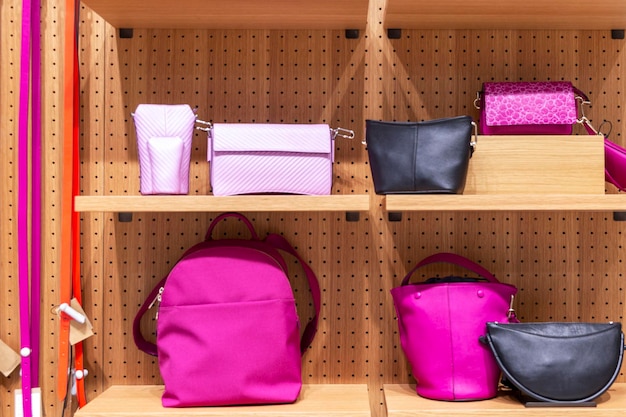 Bright women's bags and belts in different shades of pink on the wooden shelves of a shop window Fashion style and comfort Front view