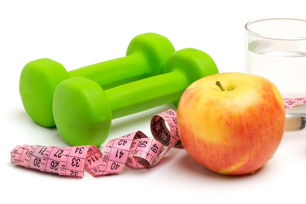 Photo bright yellow apple with a glass of water and red dumbbells, measuring tape on white