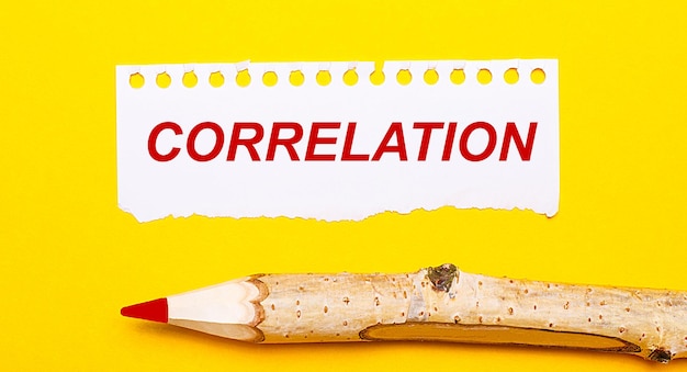 On a bright yellow background a large wooden pencil and a sheet of torn paper with the text CORRELATION