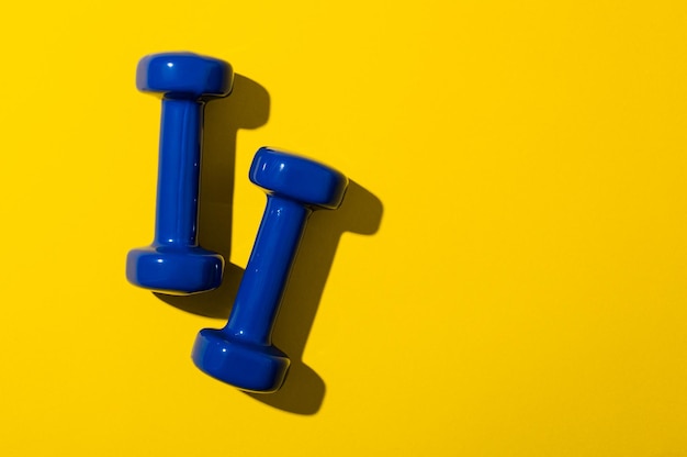 On a bright yellow background, two blue dumbbells for fitness. Copy space. Banner. Sport and fitness concept