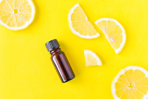 Bright yellow background with lemon slices and citrus oil in a brown glass bottle