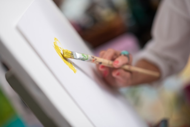 Bright yellow. Close up of painting brush with bright yellow gouache in hands of artist