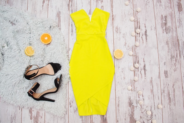 Bright yellow dress, black shoes, and citrus on the fur. Lanterns, Light wooden background. Fashionable concept, top view