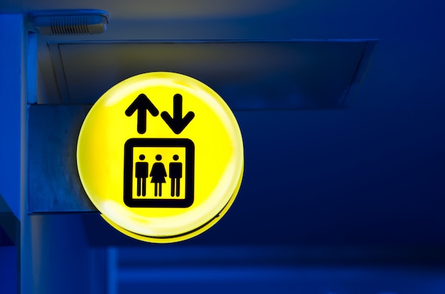 Bright yellow lift or elevator symbol, sign on blue wall background with neon light. Copy space