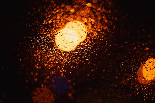 Bright yellow lights and bokeh with raindrops on the window on\
street on black background