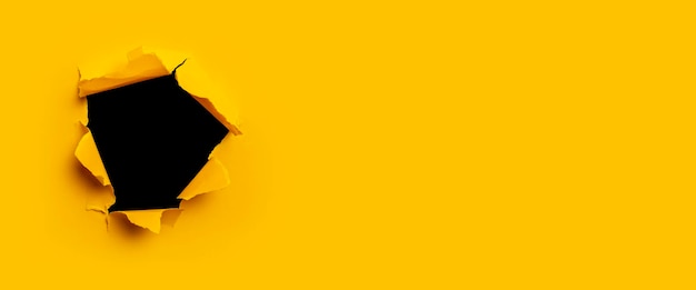Photo bright yellow torn paper inside a black hole in a hole. banner.