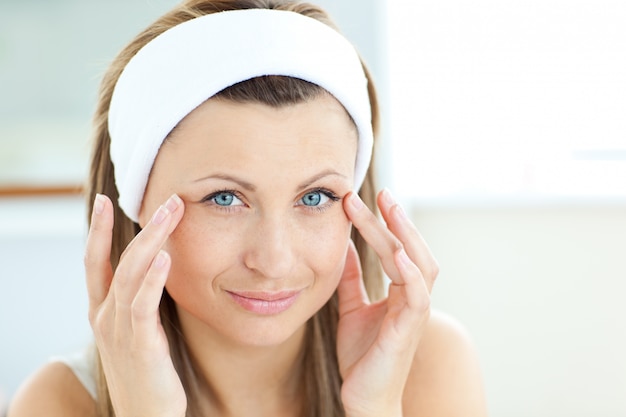 Bright young woman putting cream on her face in the bathroom at home