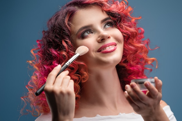 Bright young woman with makeup brush curly red hair