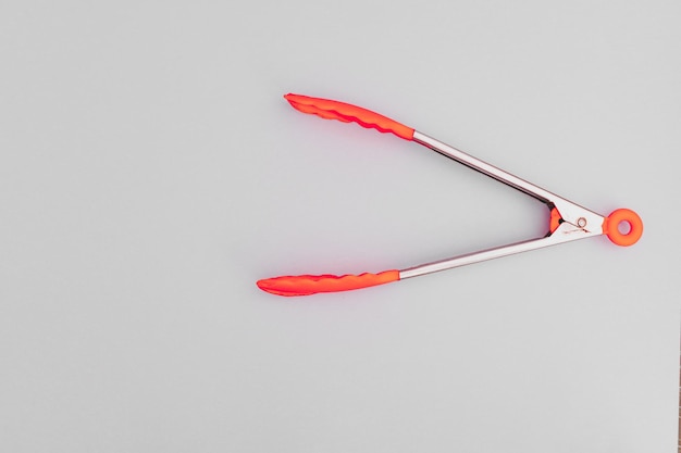 The brightly coloured pasta tongs lie on a pink background