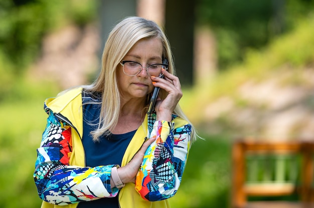 Brightly dressed blonde mature woman talking on smartphone in garden online communication concept