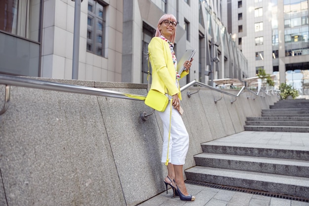 Brightly dressed lady carrying laptop while staying on stairs