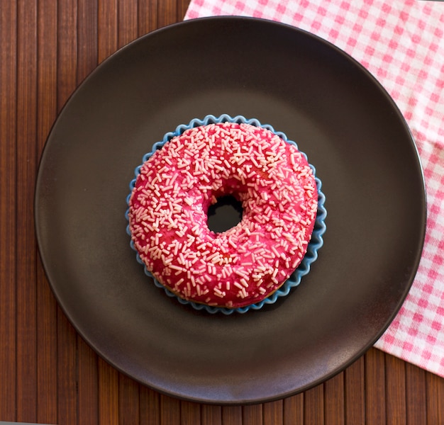 Brightly pink donut on a black ceramic plate 