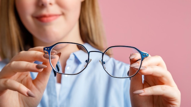 Brillen in handen Blauwe modieuze metalen bril voor visie in handen van lachende jonge vrouw Ooggezondheid Controle van zichtcorrectie via brillen over roze kleur achtergrond Lange webbanner