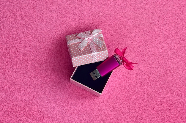 Блестящая розовая флешка с розовым бантом лежит в небольшой подарочной коробке в розовом