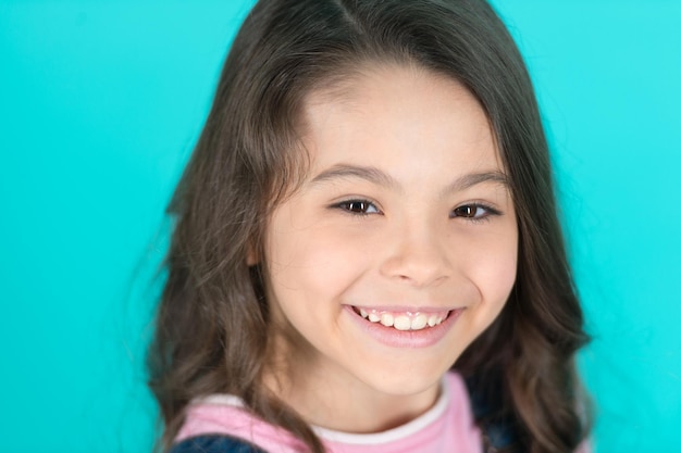 Brilliant smile Kid happy carefree enjoy childhood Child charming brilliant smile turquoise background Kid girl long curly hair cheerful happy Girl curly hairstyle adorable smiling face