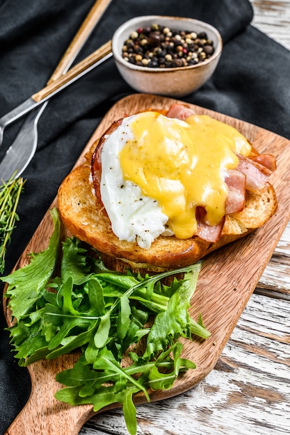 Brioche sandwich with bacon, egg Benedict and hollandaise sauce. White background. Top view