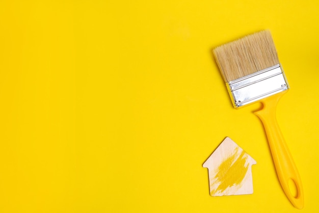 黄色の背景に家の置物と同様に塗装と修理のための毛のペイントブラシ