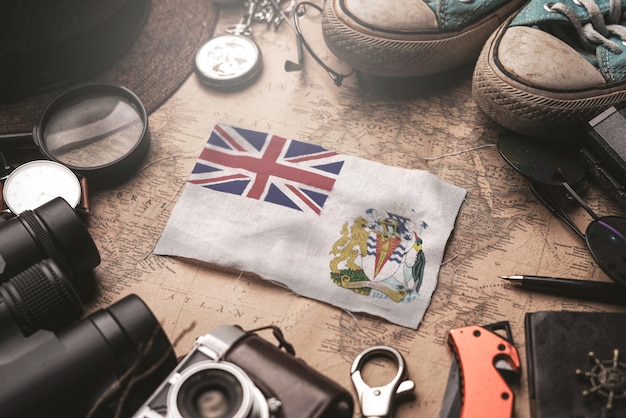 写真 古いビンテージマップ上の旅行者のアクセサリーの間にイギリスの南極地域の旗。観光地のコンセプト。