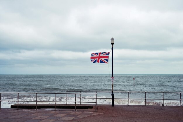 Photo british flag on sidewalk by sea against cloudy sky