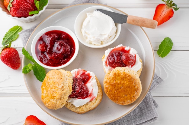 British Scones with cream cheese strawberry jam and a cup of tea on a white wooden background