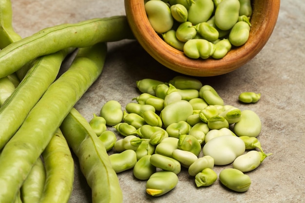 Broad beans in a wooden bowl and on a marble table