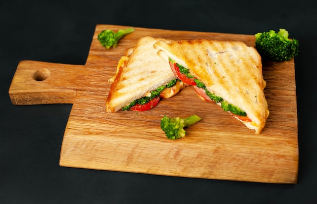 Broccoli cheese sandwiches on wooden cutting board, on concrete, slate background