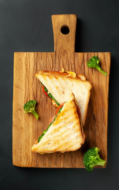 Broccoli cheese sandwiches on wooden cutting board, on concrete, slate background