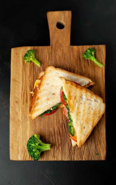 Broccoli cheese sandwiches on wooden cutting board, on concrete, slate background