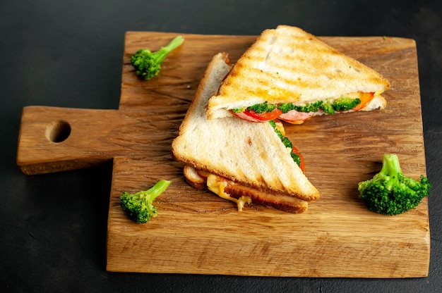 Broccoli cheese sandwiches on wooden cutting board, on concrete, slate background