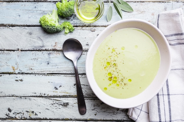 Broccoli cream soup in white bowl on wooden background, top view