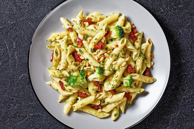 Broccoli pesto penne pasta met zongedroogde tomaten en pijnboompitten op een bord, horizontale weergave van bovenaf, Italiaanse keuken, close-up, plat gelegd