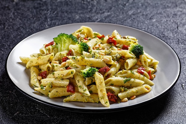 Broccoli pesto penne pasta met zongedroogde tomaten en pijnboompitten op een bord, horizontale weergave van bovenaf