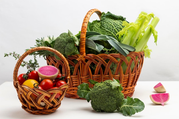 Broccoli and pink radish on table. Two wicker baskets with vegetables and greens. White background.