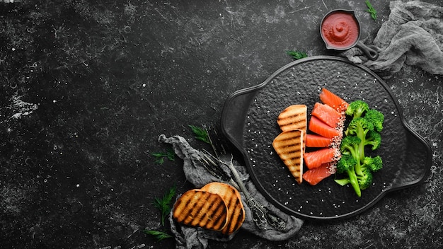 Broccoli and salted salmon fish Healthy Diet Food On a black stone plate Top view