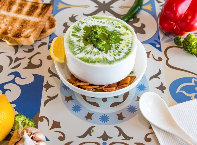 Broccoli Soup with lemon crackers spoon and bell pepper served in dish isolated on table top view of arabic food